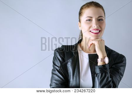 portrait of beautiful young brunette woman in stylish black jacket on gray.