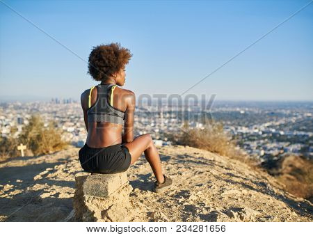 athletic african american woman resting at top of runyon canyon looking at view of los angeles cityscape