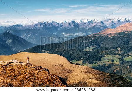 Young Man Hiker In Bright Jacket Stands On Cliff At Mountains Dolomites And Takes Photography Of Val