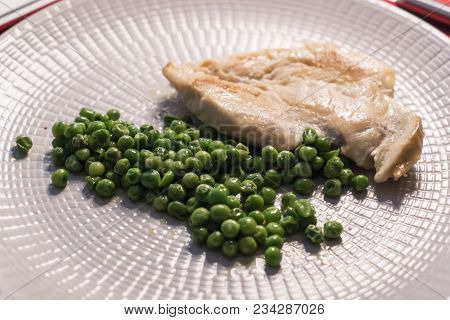 A Grilled Chicken Breast With Peas In The Dish