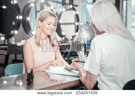 Professional Manicure. Cheerful Delighted Happy Woman Looking At Her Hands And Smiling While Having 