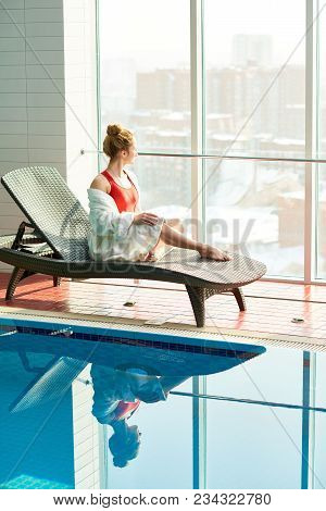 Full Length Portrait Of Beautiful Young Woman Relaxing Sitting In Wicker Lounge Chair By Swimming Po