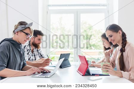 Side view of four dedicated young people sharing a desk while telecommuting in a modern co-working space for freelancers and independent contractors 