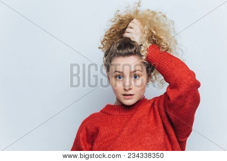 Indoor Shot Of Beautiful Blue Eyed Female In Red Sweater, Poses With Stunned Expression, Dressed In 