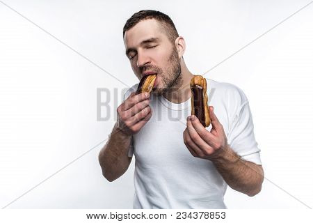 Strong And Well-built Guy Is Standing And Eating Eclair. Also He Has Another Eclair In The Other Han