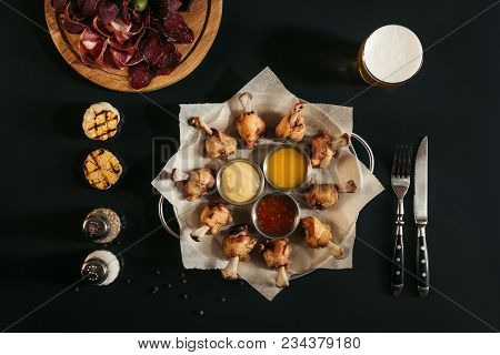 Top View Of Delicious Roasted Chicken With Various Sauces On Baking Paper And Glass Of Beer On Black