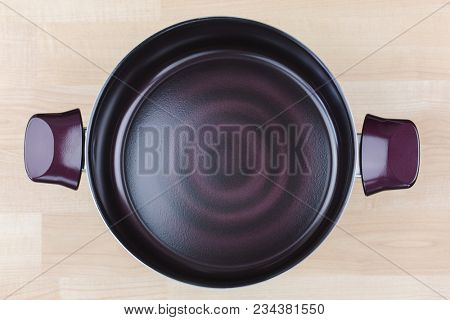 Large coated Stewpot, cooking pot in dark purple ruby color. Cookware with induction technology on wood background, top view