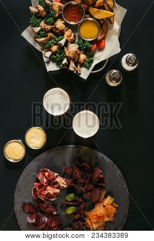 Top View Of Glasses Of Beer, Assorted Meat And Fried Potatoes With Chicken On Black