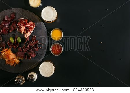 Top View Of Delicious Sliced Assorted Meat, Glasses Of Beer, Sauces And Spices On Black
