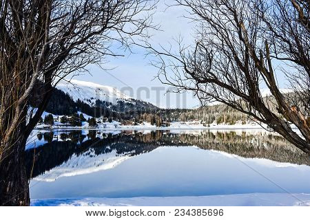 Lake Davos In Switzerland, With Blue Sky Reflected In Its Crystal Clear Waters Surrounded By Snow An