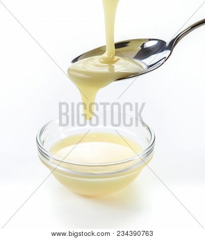 Closeup Pouring Condensed Milk With Teaspoon On White Background