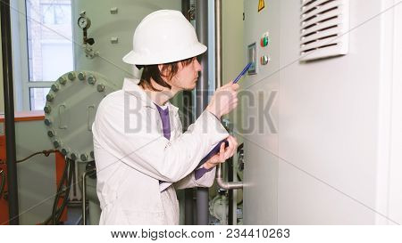 The White Helmet Engineer Records The Readings From The Display Of The Electric Control Cabinet And 