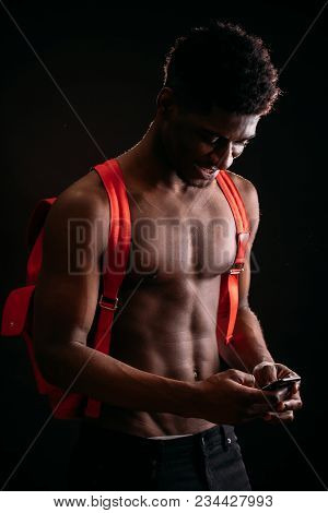 Side View Close Up Image Of Smiling Nude African Male With Pinck Bag Standing With Mobile Phone. Cha