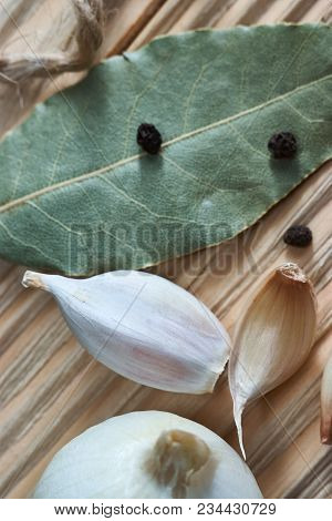 Onion, Garlic, Black Pepper And Bay Leaf On A Wooden Table