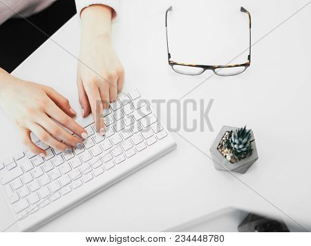 White Office Table And Woman Working On Computer. Top View. Typing On Keyboard