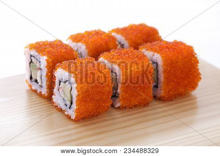 One Set Of California Rolls Covered Orange Tobiko Or Masago Caviar On A Wooden Board On A White Back