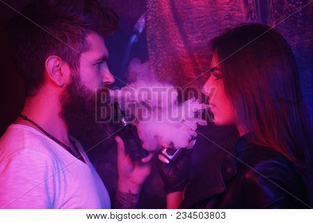 Young Man And Woman Blowing Smoke To Join It In One Cloud At Black Studio Background. Relationship A