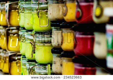 Glass Jars With Colorful Sauces Stand In A Row On The Shelves Of The Supermarket