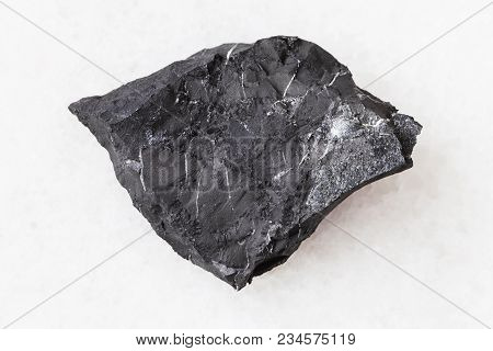 Macro Shooting Of Natural Mineral Rock Specimen - Piece Of Shungite Shale Stone On White Marble Back