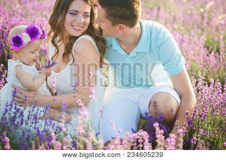 Mom, Dad And Their Little Daughter In A Beautiful Wreath Are Walking In A Lavender Field. Life In Pr