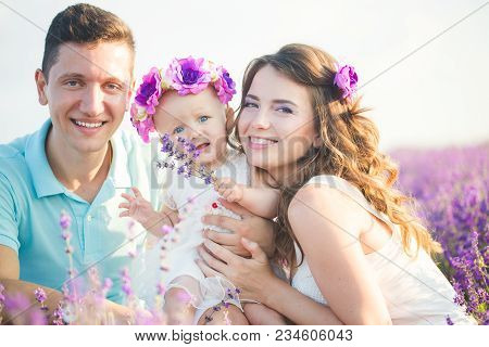 Mom, Dad And Their Little Daughter In A Beautiful Wreath Are Walking In A Lavender Field. Life In Pr