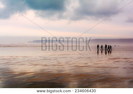 Group Of People Walking On A Sandy Beach In Wet Weather