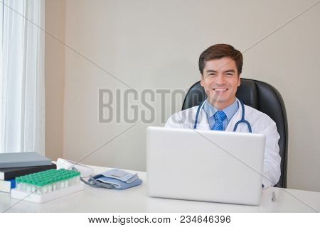 Smiling Doctor Posing In The Office, He Is Wearing A Stethoscope, Medical Staff On The Hospital Back