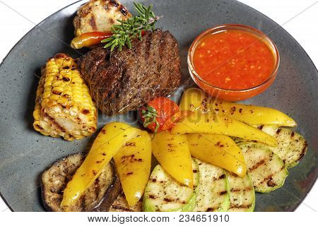 Fried Meat With Garnish Of Pepper, Zucchini, Tomato And Corn With Ajika Sauce Served On A Gray Plate