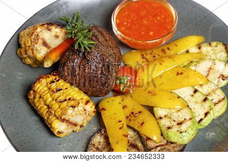 Fried Meat With Garnish Of Pepper, Zucchini, Tomato And Corn With Ajika Sauce Served On A Gray Plate