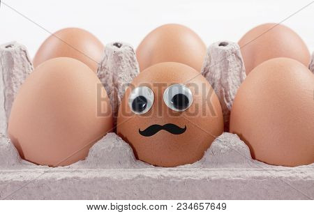 Close-up Of Raw Chicken Eggs In A Box. Funny Egg With Eyes And A Mustache Concept. Macro.