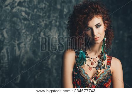 Beautiful bright woman with curly foxy hair wears a dress and beads in boho style. Ethnic style in clothes.
