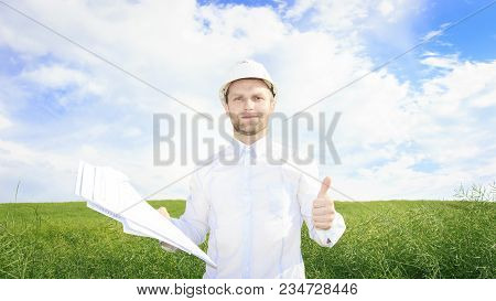 Engineer Builder With Drawings In Hands On Green Meadow. Pedologist In White Helmet On Green Summer 