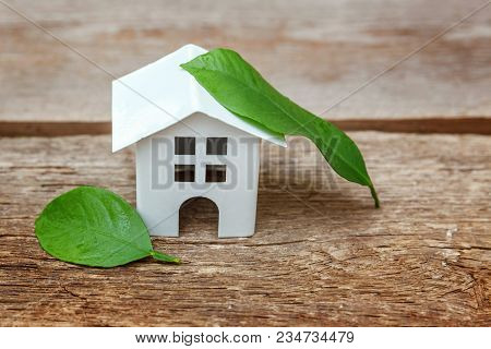 Miniature White Toy Model House With Green Leaves On Wooden Backgdrop. Eco Village, Abstract Environ