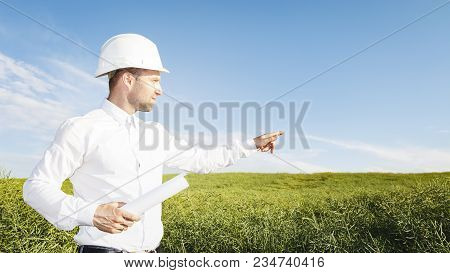 Builder Geodesist In White Helmet With Drawings Points Place Of Construction Of Object. Engineer On 