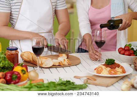 Cropped Image Of Man Cutting Bread And His Girlfriend Is Poring Red Wine