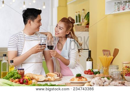 Joyful Young Asian Couple Drinking Tasty Red Wine In Kitchen