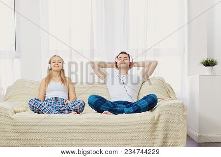 Couple In Headphones Lying On Sofa Listening To Music In Room On Window Background.