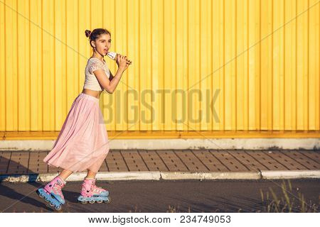 Young Girl On Hot Day Roller-skating And Eating Ice Cream On Yellow Wall Background. Concept Of Heal