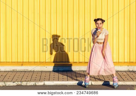 Young Girl Roller-skating And Eating Ice Cream On A Yellow Wall Background. Life Style. Copy Space.
