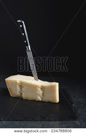 An Appetizing Solid Cheese On A Black Plate On A Gray Stone Background