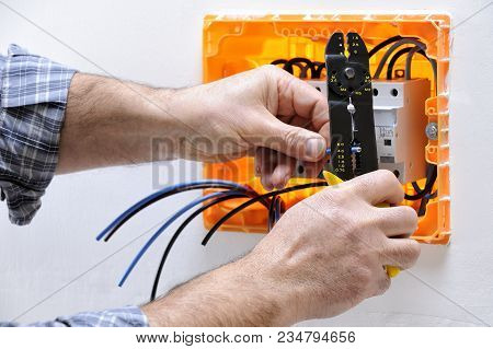 Electrician Technician At Work On A Residential Electric Panel, Prepares The Cable With A Wire Strip