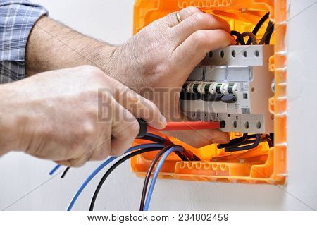 Electrician Technician Working On A Residential Electrical Panel, Fixing With A Screwdriver The Cabl