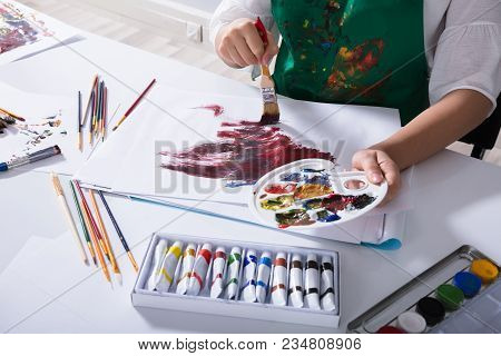 Artist Holding Paint Palette While Painting On Canvas Paper
