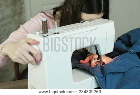 Young Woman Sews Blue Jacket On White Sewing Mashine