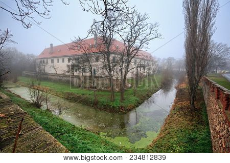 The Moated Manor House In The Market Town Of Guntersdorf On A Foggy Winter Day. District Of Hollabru