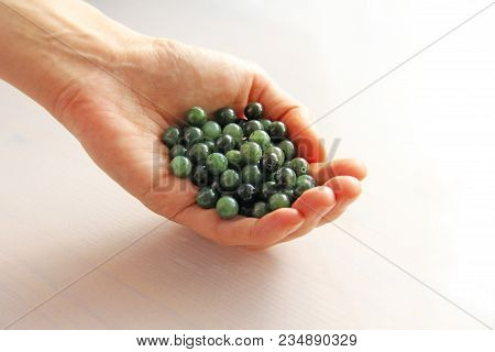 Natural Green Jade Nephrite Mineral Stones Beads. The Green Jade Stone Lies In The Hands. Hands Hold