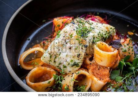 braised codfish filet and lettuce, herbs with calamarata noodles as top view on a plate