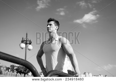 Man Bodybuilder Posing On Blue Sky. Athlete In Green Tshirt On Sunny Day. Fitness Model With Muscula