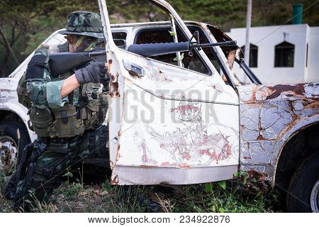 Special Forces Soldier Or Private Millitary Holding Gun Aiming Behind A Dilapibated Car At Field Are