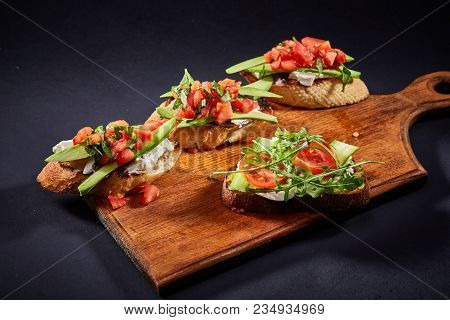 Grilled Toast Brisket With Tomato, Avocado And Ruccola On Wooden Cutting Board Over Dark Background,